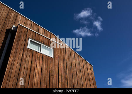 Architectural features of a modern house with wood cladding and a window against a blue sky with a cloud. Stock Photo