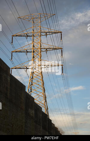 Electrical metal power line pylon isolated in the morning light against a blue cloudy sky distributing energy in the modern suburban environment. Stock Photo