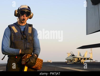 ARABIAN GULF (Sept. 22, 2017) U.S. Navy Aviation Boatswain’s Mate (Handling) Airman Christopher Adams, from Hartford, Vt., prepares to move a plane on the flight deck aboard the aircraft carrier USS Nimitz (CVN 68), Sept. 22, 2017, in the Arabian Gulf. Nimitz is deployed in the U.S. 5th Fleet area of operations in support of Operation Inherent Resolve. While in this region, the ship and strike group are conducting maritime security operations to reassure allies and partners, preserve freedom of navigation, and maintain the free flow of commerce. Stock Photo