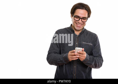Studio shot of young happy Persian man smiling while using mobil Stock Photo