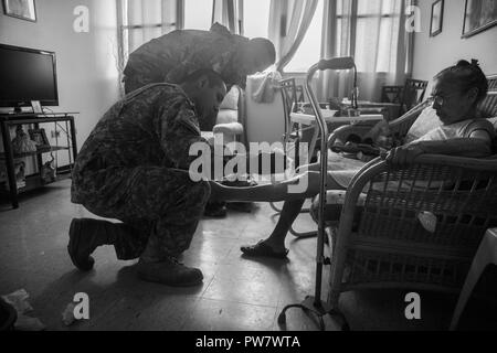 U.S. Army Sgt. Luis Rodriguez, left, a flight medic, and Capt. Benjamin Stork, rear, a flight surgeon, both assigned to 101st Combat Aviation Brigade (CAB), 101st Airborne Division (Air Assault), check a leg rash on Georgina Felix, a resident of Edificio Franciso Colon Gordian, a home for elderly care, in Ceiba, Puerto Rico, Sept. 30, 2017. The 101st CAB is conducting medical evacuation and relief efforts to support FEMA in the recovery process of Puerto Rico after the devastation created by Hurricane Maria. Stock Photo