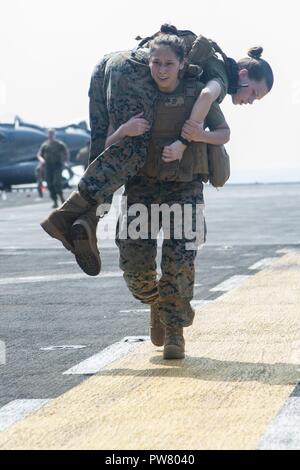 5TH FLEET AREA OF OPERATIONS (Sept. 28, 2017) Marine Corps Sgt. Raven Mitchell, a native of Woodsboro, Texas, carries Marine Corps Cpl. Amanda Barnes, a native of Panama City, Florida, over her shoulder during a combat endurance training drill on the flight deck of the amphibious assault ship USS America (LHA 6). America is the flagship for the America Amphibious Ready Group and, with the embarked 15th Marine Expeditionary Unit, is deployed to the U.S. 5th Fleet area of operations in support of maritime security operations to reassure allies and partners and preserve the freedom of navigation  Stock Photo