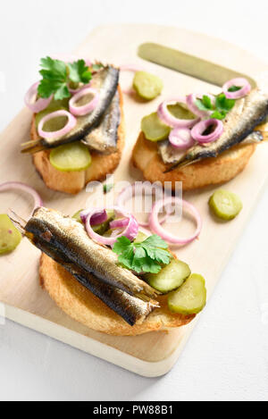 Tasty sandwiches with sprats, marinated cucumber and onion on wooden board over white  background. Stock Photo