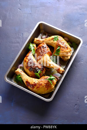 Grilled chicken legs in baking tray on blue stone background.