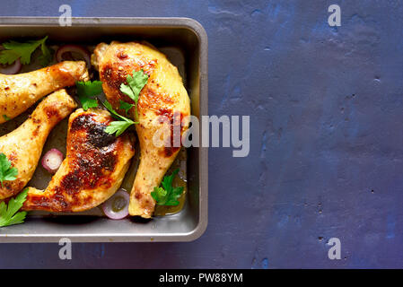 Roasted chicken legs in pan on blue stone background with copy space. Top view Stock Photo