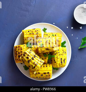 Homemade grilled corn on the cob on plate over blue stone background. Top view Stock Photo