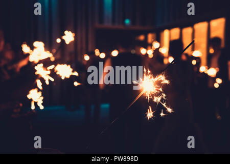 Close up of a bengal light at the blurred background of people standing with burning sparklers in semidarkness. Indoor firework by the turned off ligh Stock Photo