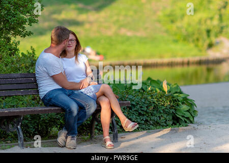 RIGA, LATVIA - JULY 26, 2018: Embracing young people sits on a bench in the park. Stock Photo