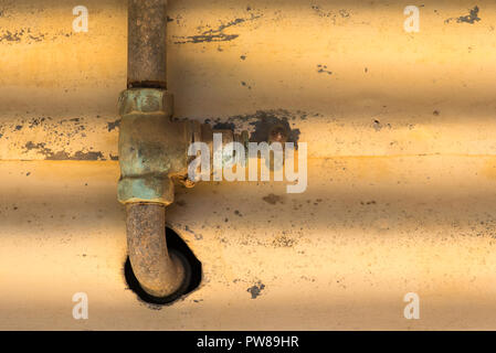 An old rusty pipe and tap running up and through a hole in a wall Stock Photo