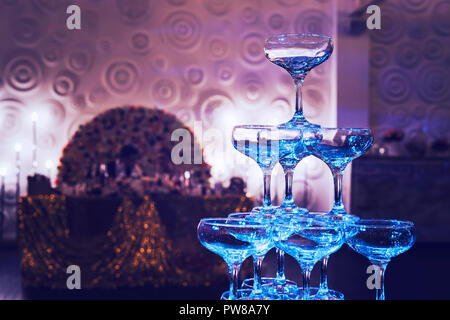 Awesome shot of glittering 3-tier champagne tower at the decorated banquet hall background. Beautifull built-in set of coupe glasses at a wedding room Stock Photo