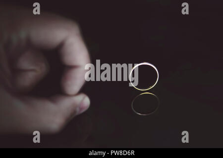Close up of man's fingers on the reflecting black surface pushing on the wedding ring at the black background. Male hand on the black table near the g Stock Photo