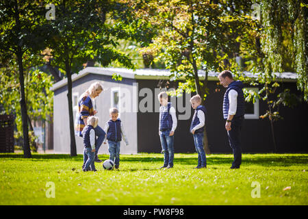 The theme family outdoor activities. big friendly Caucasian family of six mom dad and four children playing football, running with the ball on lawn, g Stock Photo