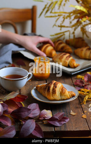 Cozy Autumn Still Life, Fall Breakfast, Freshly Baked Croissants with Cinnamon and Salted Caramel, Cup of Tea and Autumn Leaves on Wooden Table Stock Photo