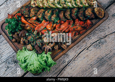 Fried grilled vegetables on a wooden board, along with leaves of green salad. Stock Photo