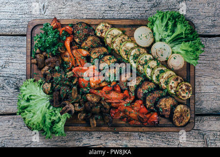 Fried grilled vegetables on a wooden board, along with leaves of green salad. Stock Photo