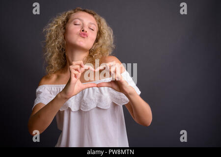 Young beautiful woman with blond curly hair against gray backgro Stock Photo