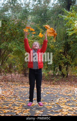 A girl with special needs jumping on a background of autumn forest throws up yellow leaves Stock Photo