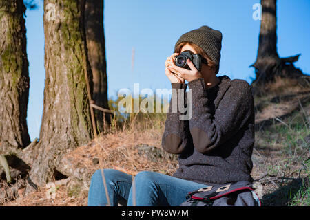 Taking a photo with an old analog camera in the forest. Female hiker using a camera in beautiful nature scene on bright sunny day Stock Photo