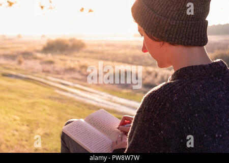 Writing a diary in beautiful nature. Woman facing evening sun takes notes into a notepad Stock Photo