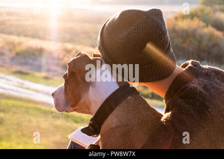 Hugging a dog in beautiful nature at sunset. Woman facing evening sun sits with her pet next to her Stock Photo