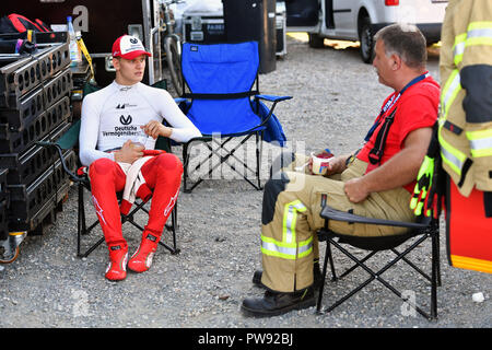 Hockenheim, Deutschland. 13th Oct, 2018. Mick SCHUMACHER, (GER, PREMA Theodore Racing) sits next to a firefighter in a camping chair and talks to him. Fia Formula 3 European Championships, Formula 3, at the Hockenheimring on 13.10.2018. | usage worldwide Credit: dpa/Alamy Live News Stock Photo