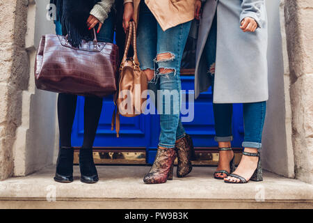 Three women wearing stylish shoes and accessories outdoors. Autumn fashion concept. Ladies holding modern female handbags Stock Photo