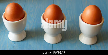 3 boiled eggs in white egg cups on a blue wooden background Stock Photo