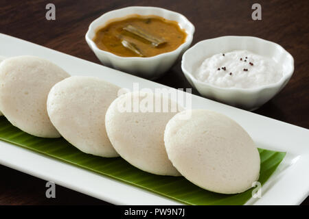 Fresh steamed Indian Idly (Idli / rice cake) arranged on banana leaf lined plate. Served with coconut chutney and sambar. Natural light used. Stock Photo