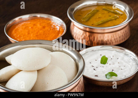 Fresh steamed Indian Idly (Idli / rice cake) arranged in authentic copper bowl. Served with tomato chutney, coconut chutney and sambar. Natural light. Stock Photo