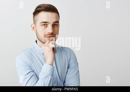 Waist-up shot of smart creative male boss in formal blue shirt being ambitious and optimistic holding hand on chin smiling thoughtfully having interesting plan how level up company income Stock Photo