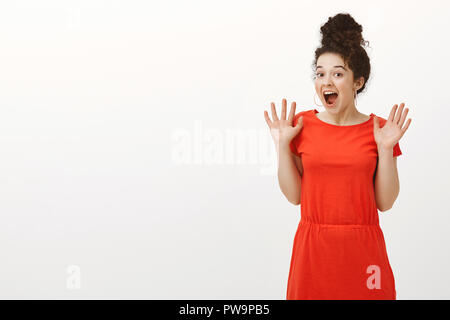 Portrait of happy excited caucasian curly-haired girl with bun haircut, smiling broadly and screaming from amazement and surprise, raising palms, reacting happily to amazing unexpected present Stock Photo