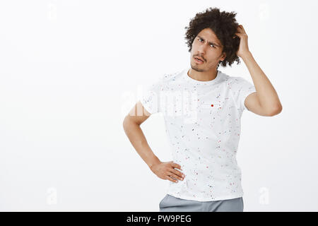 I do not get it. Portrait of stupid handsome sportsman with afro hairstyle and moustache, tilting head, scratching and staring with dumb expression and opened mouth at camera, cannot understand Stock Photo