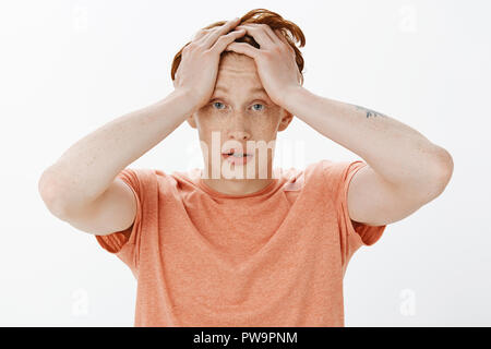 Redhead man feeling headache when girlfriend starting whining, holding hands on head and gasping, gazing with tired and gloomy expression at camera, standing exhausted and fed up over grey wall Stock Photo
