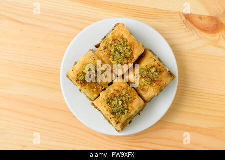 Top view of mouthwatering Baklava pastries topped with pistachio nuts on a white plate served on light brown wooden table Stock Photo