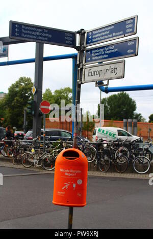 Blue street sign pointing to Berlin tourist attractions like Brandenburg Gate and Reichstag, with orange litter bin and bicycles in the background Stock Photo