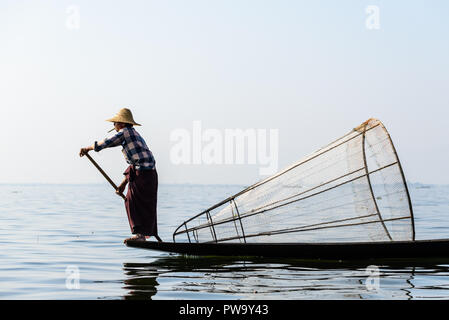 INLE LAKE, MYANMAR - FEBRUARY 15, 2014: Burmese fisherman on bamboo boat catching fish in traditional way with handmade net. Inle lake, Myanmar (Burma Stock Photo