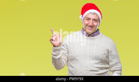 Handsome senior man wearing christmas hat over isolated background with a big smile on face, pointing with hand and finger to the side looking at the  Stock Photo