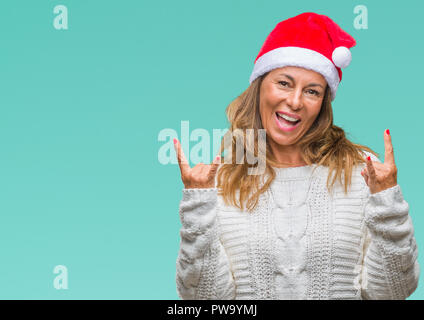 Middle age senior hispanic woman wearing christmas hat over isolated background shouting with crazy expression doing rock symbol with hands up. Music  Stock Photo