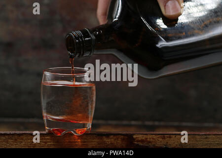 rum is poured from bottle into a shot glass, served on dark wooden background Stock Photo