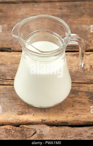 Transparent jug with milk on wooden background. Fresh organic milk in glass jug on rustic wooden boards. Stock Photo