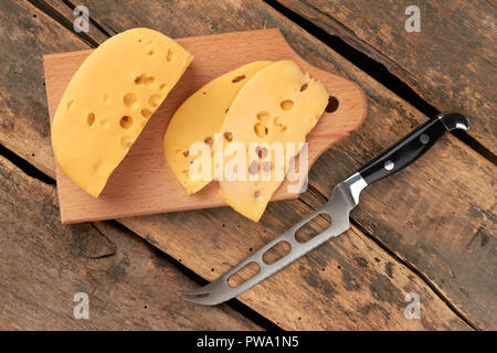 Traditional Dutch cheese with holes. Slices of Maasdam chees and knife on vintage wooden boards. Healthy dairy product. Stock Photo