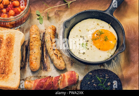 Full english fry up breakfast with egg, sausages, black pudding, baked chickpeas and toasts as culinary background Stock Photo