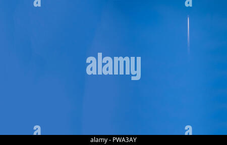 A jet airplane far away climbing fast with a long double white trail in a pretty clear blue sky Stock Photo