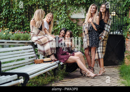 Six beautiful girls wrapped in plaid posing on camera in park on bench Stock Photo