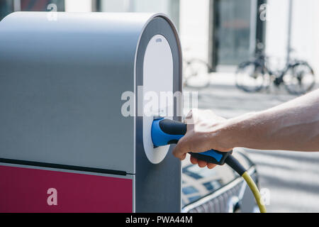 Close-up of a hand inserts a special cord or cable into an outdoor refueling station for refueling an electric car. Eco-friendly mode of transport. Stock Photo