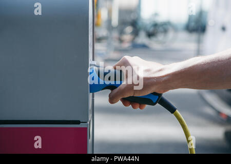 Close-up of a hand inserts a special cord or cable into an outdoor refueling station for refueling an electric car. Eco-friendly mode of transport. Stock Photo