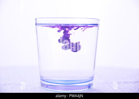Glass with water on a white background with purple paint Stock Photo