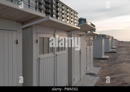 Row of white beach huts on the sand in front of seafront apartment buildings in Ostend, Belgium Stock Photo