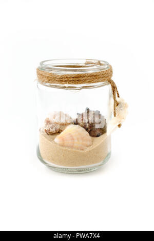 Seashells and sand in a handmade glass jar decorated with mini seashells and isolated on white background. Low angle view. Stock Photo