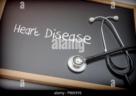 Word Heart Disease written in chalk on a blackboard black next to a stethoscope, conceptual image Stock Photo